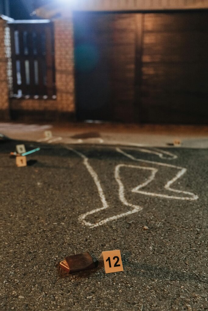 Chalk outline and evidence markers at a crime scene outdoors at night.